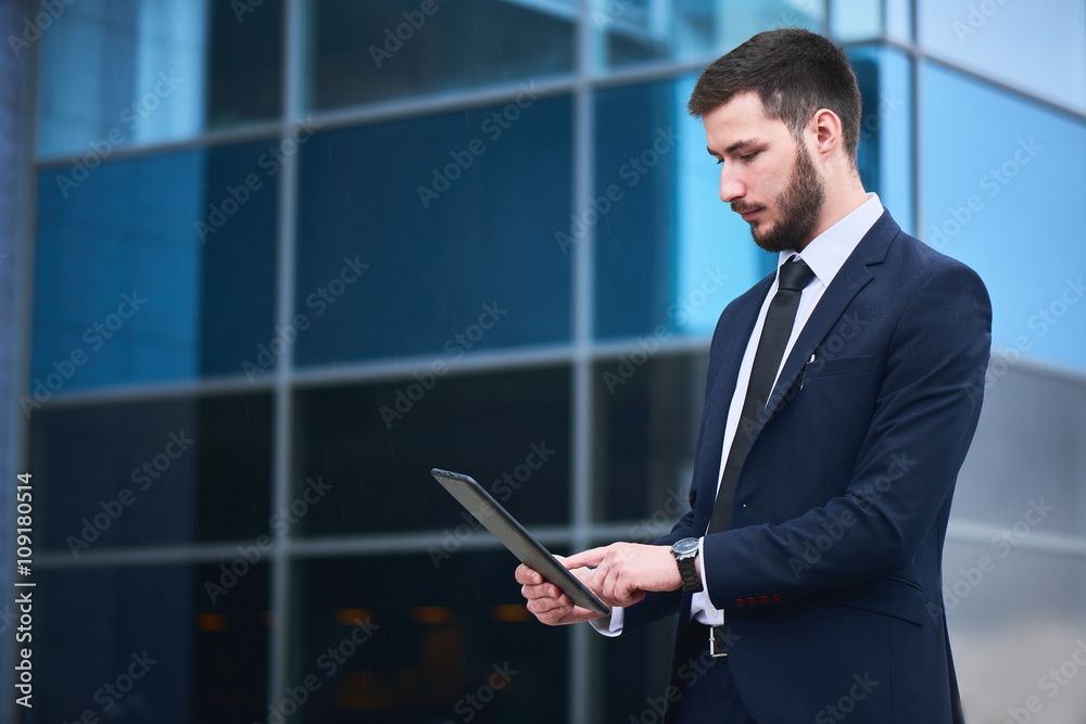 Businessman holding tablet on background of buildings with glass facades Businessman holding tablet on background of buildings with glass facades