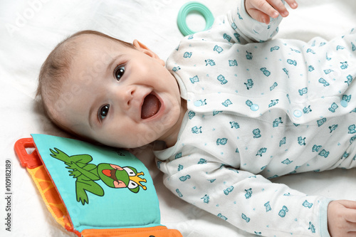 Cute smiling infant lying in his bed with different toys