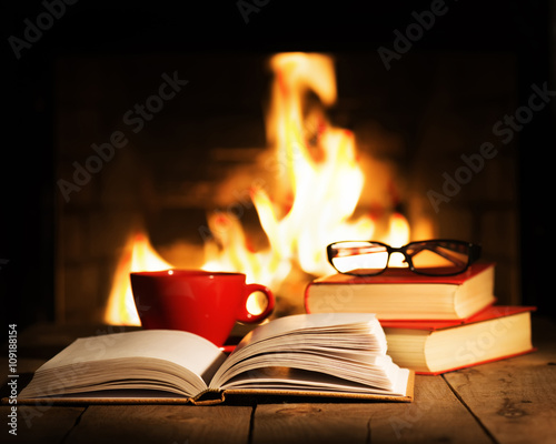 Red cup and old books on wooden table near fireplace.