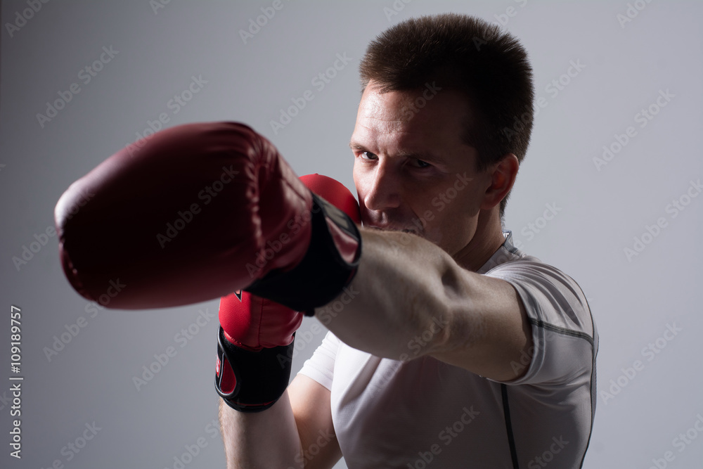 Close-up portrait of boxer in red boxing gloves on a gray background.