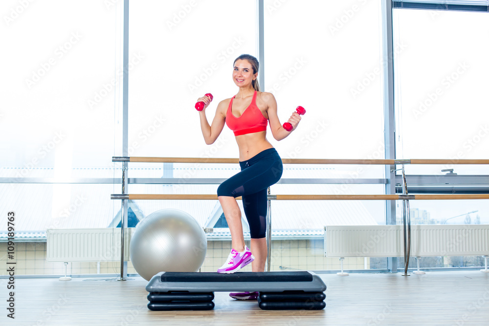 Fototapeta premium girl performs step cardio with dumbbells in a gym