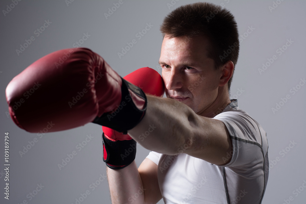 Close-up portrait of boxer in red boxing gloves on a gray background.