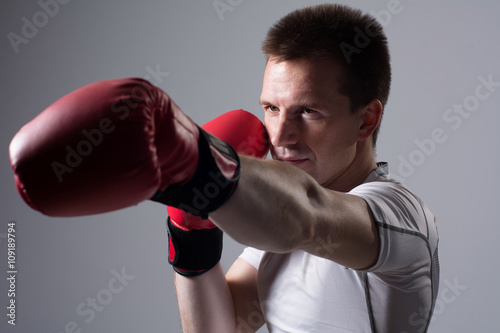 Close-up portrait of boxer in red boxing gloves on a gray background. © kanzefar