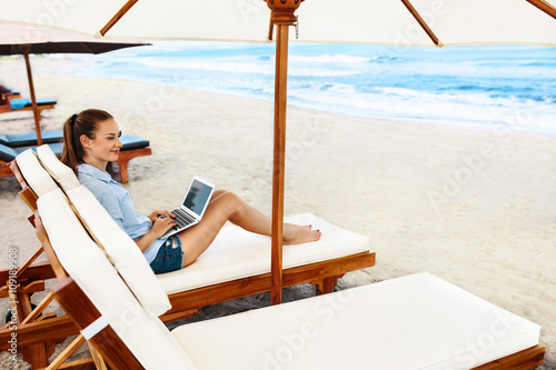 Beautiful Business Woman Working Online On Laptop Computer While Lying On Beach Lounger. Happy Smiling Freelancer Girl Relaxing And Using Notebook For Freelance Internet Work. Communication Technology © puhhha