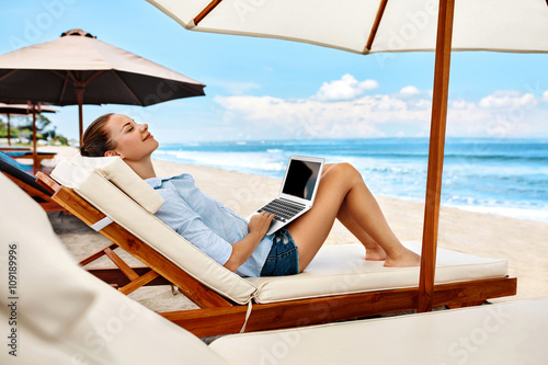 Beautiful Business Woman Working Online On Laptop Computer While Lying On Beach Lounger. Happy Smiling Freelancer Girl Relaxing And Using Notebook For Freelance Internet Work. Communication Technology © puhhha