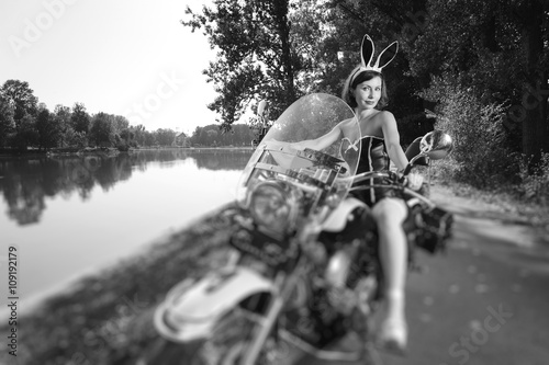 Young beautiful sexy bunny-girl sitting on cruiser motorcycle near the lake. Hot summer day. Tilt shift lens blur effect. black and white