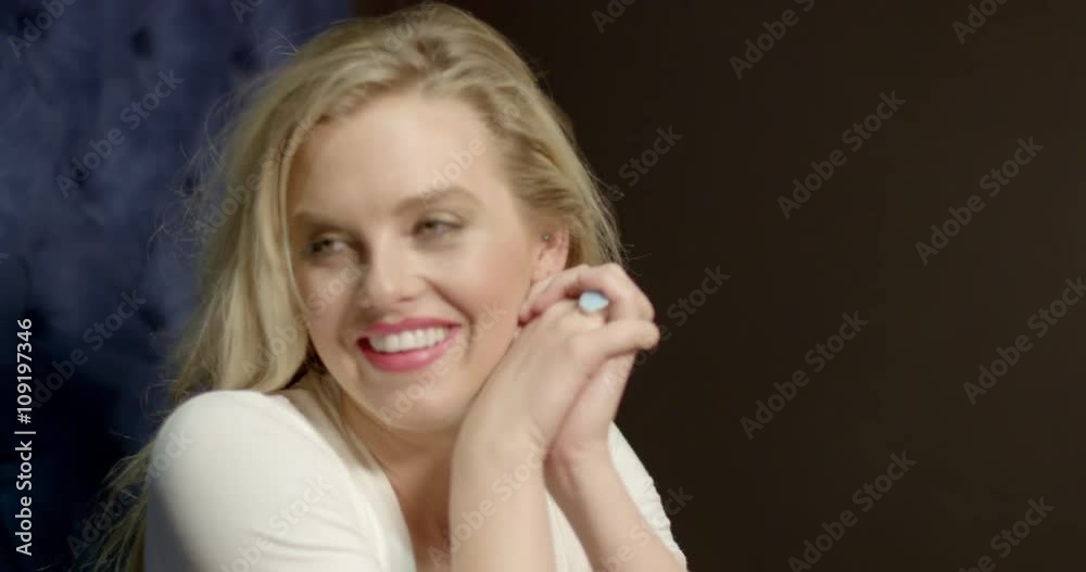 Close up of beautiful young blonde woman sitting on big blue sofa seat and laughing, going in and out of focus. Hand held, slow motion, recorded in 4K at 60fps.