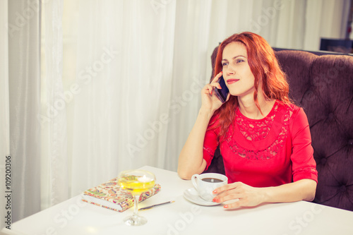 Beautiful woman using laptop, phone at table in cafe.