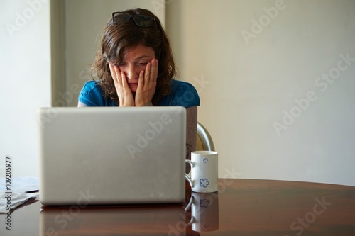 Young woman sitting at table using laptop, looking stressed