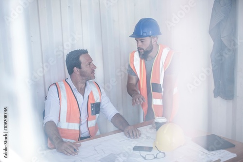 Tablou pe pânză Construction foreman and builder meeting at desk in portable cabin