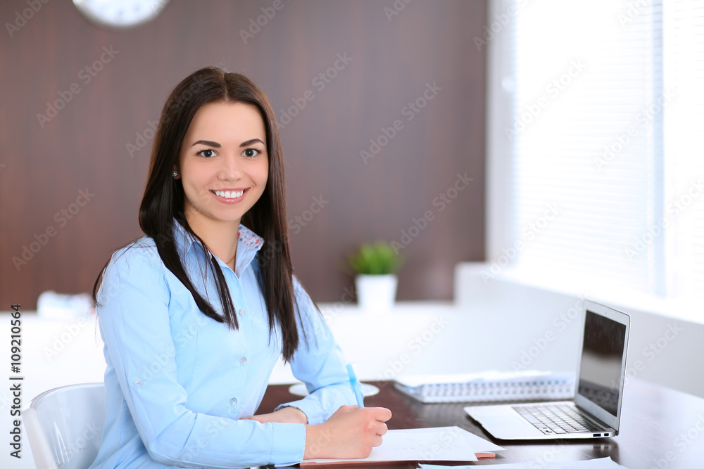 Young business woman sitting and writing at the table in office Young business woman sitting and writing at the table in office