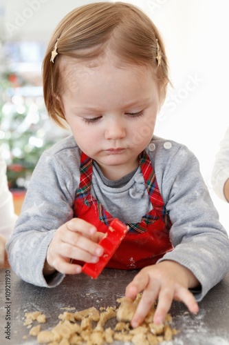 Girl holding cookie cutter looking down touching cookie dough photo