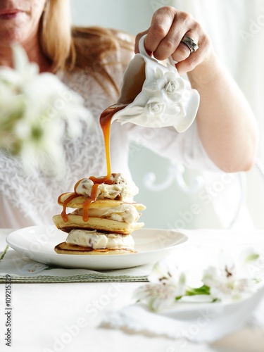 Woman pouring toffee sauce from ornate jug on stack of pikelets photo