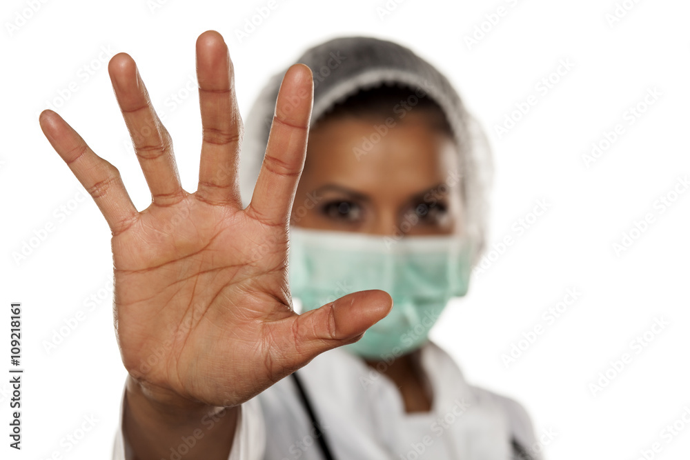 portrait of a young doctor with a hat and a mask showing stop with her hand portrait of a young doctor with a hat and a mask showing stop with her hand