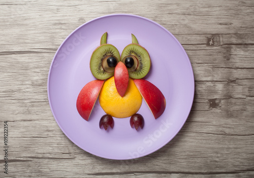Owl made of fruits on plate and wooden background