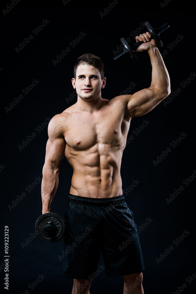 Perfect fit athletic guy posing with barbell plate in gym, perfect lat muscle, shoulders, biceps, triceps and chest. Fitness muscular body isolated on dark background.