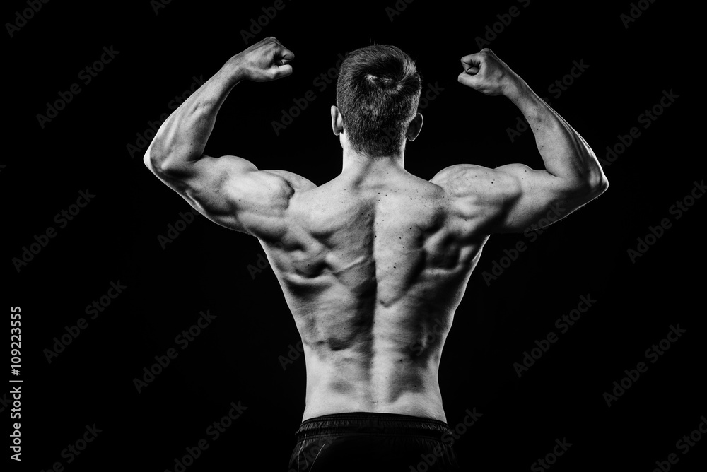 Young and fit bodybuilder athlete demonstrates biceps back view isolated on black background