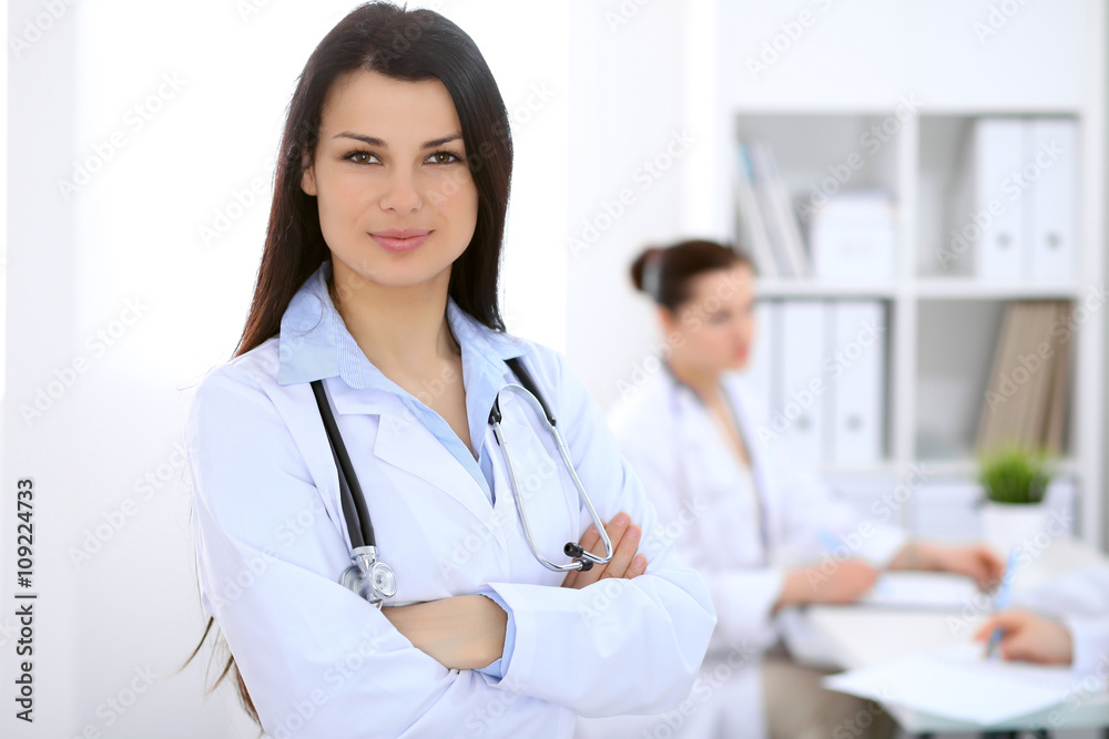 Brunette female doctor on the background of colleagues talking to each other in hospital Brunette female doctor on the background of colleagues talking to each other in hospital
