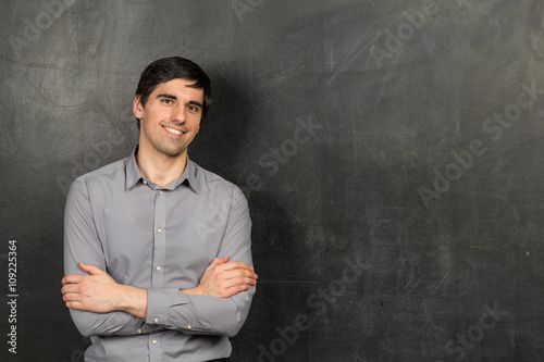 Portrait of young happy smiling teacher man standing near chalkboard background