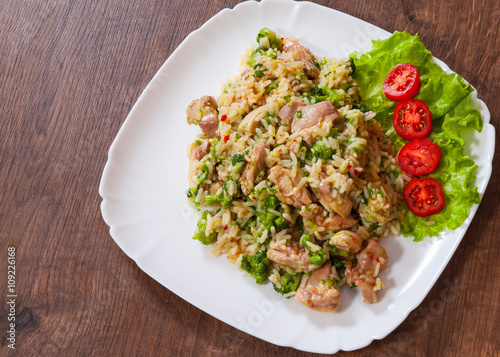 chicken meat with rice and vegetables in a plate on wooden table