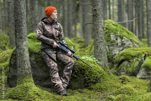 Hunter with rifle sitting on rock in forest photo