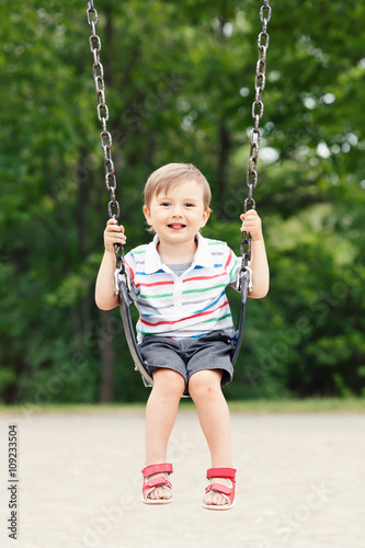 Portrait of happy smiling little boy toddler in tshirt and jeans shorts on swing on backyard playground outside on summer day, happy childhood lifestyle concept © anoushkatoronto