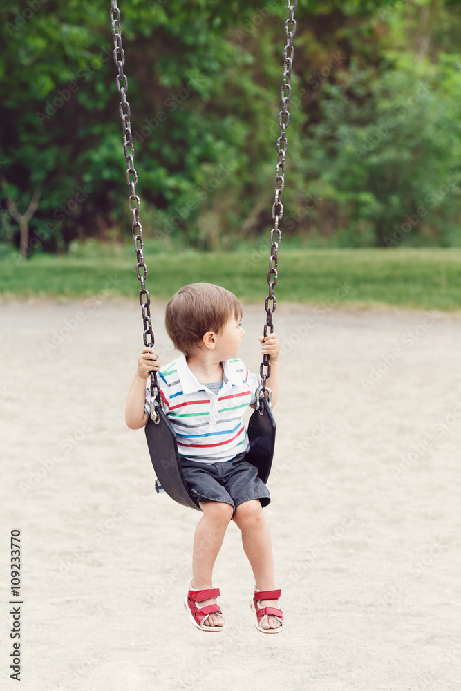 Portrait of cute little small boy toddler looking away, wearing tshirt and jeans shorts on swing on backyard playground outside on summer day, happy childhood lifestyle Portrait of cute little small boy toddler looking away, wearing tshirt and jeans shorts on swing on backyard playground outside on summer day, happy childhood lifestyle