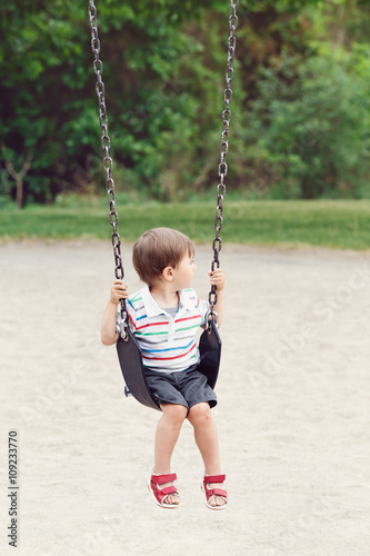 Portrait of cute little small boy toddler looking away, wearing tshirt and jeans shorts on swing on backyard playground outside on summer day, happy childhood lifestyle © anoushkatoronto