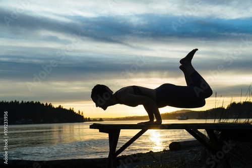 Woman practising yoga by lake at sunset