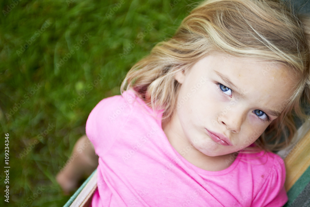 Portrait of blond child girl with blue eyes looking at camera and smiling, relaxing on a colorful hammock in a home garden on summer holiday. Vacation lifestyle kid fun activities. Portrait of blond child girl with blue eyes looking at camera and smiling, relaxing on a colorful hammock in a home garden on summer holiday. Vacation lifestyle kid fun activities.