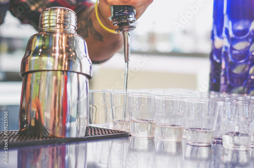 Bartender pouring alchool from the bottle in a shot glasses photo