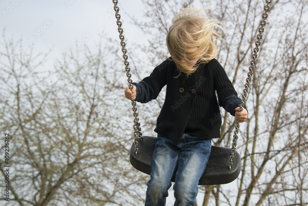 Little child blond girl having fun on a swing outdoor. Summer playground. Girl swinging high Little child blond girl having fun on a swing outdoor. Summer playground. Girl swinging high