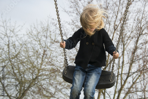 Little child blond girl having fun on a swing outdoor. Summer playground. Girl swinging high 
