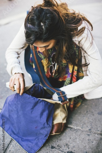 Woman crouching on pavement looking down searching though hip bag photo