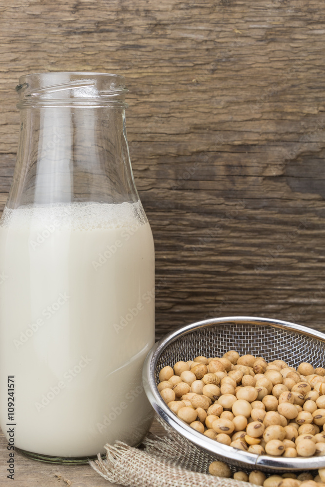 Soybeans and bottle of soy milk, on wooden background.