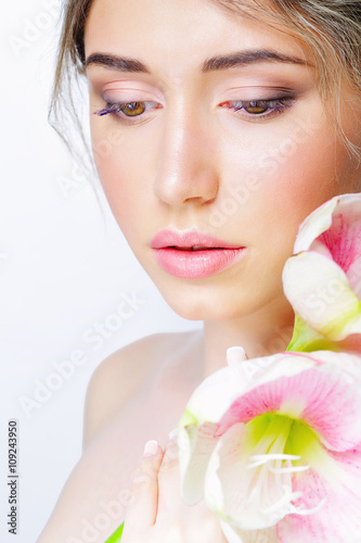 Portrait of young beautiful woman with healthy clean skin holding delicate pink flower close to her face  isolated on white background