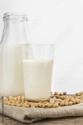 Bottle and glass of soy milk with soybeans, on white with copy-space