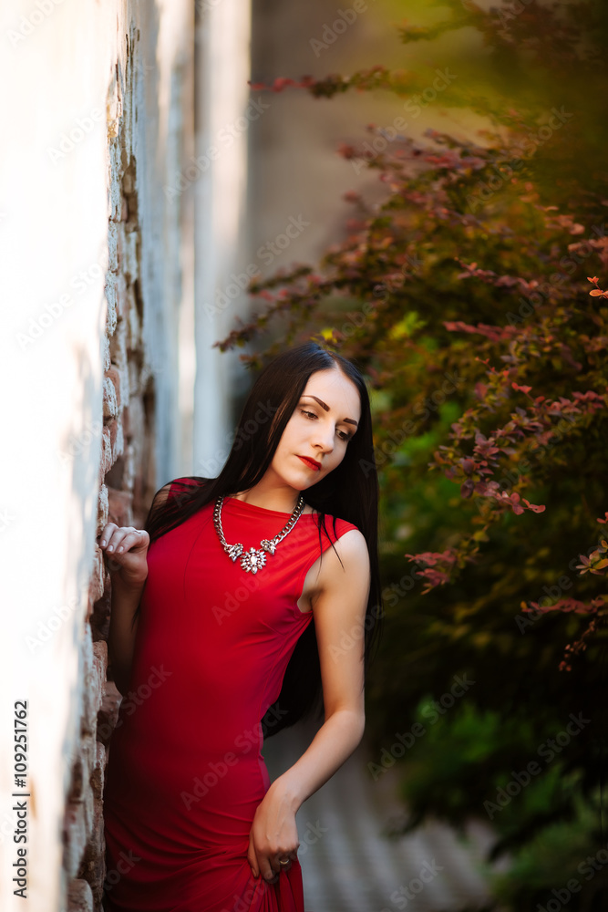 Fototapeta premium Beautiful fashionable woman outdoors. glamorous portrait of young beautiful woman in a red dress. beautiful girl portrait. Beautiful fashionable woman standing on the street. Fashion Look