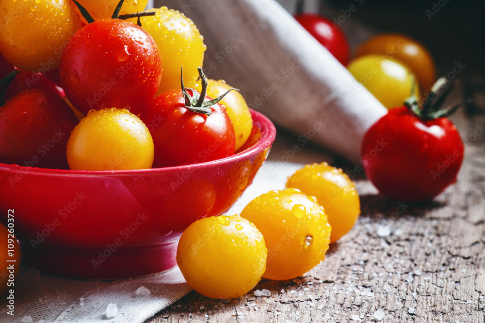 Red and orange cherry tomatoes in a red bowl, vintage wooden bac Red and orange cherry tomatoes in a red bowl, vintage wooden bac