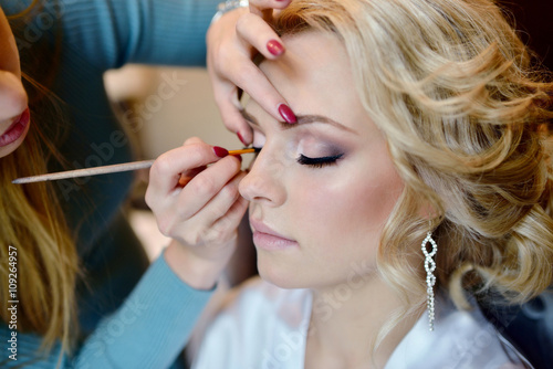 Wedding makeup artist making a make up for bride. Beautiful sexy model girl indoors. Beauty woman with curly hair. Female portrait. Bridal morning of a cute lady. Close-up hands near face