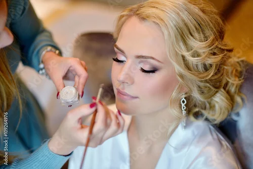 Obraz Wedding makeup artist making a make up for bride. Beautiful sexy model girl indoors. Beauty woman with curly hair. Female portrait. Bridal morning of a cute lady. Close-up hands near face