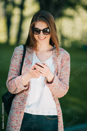 Cute caucasian young woman talking emotional and chat on the phone in the street near green park on spring sunset
