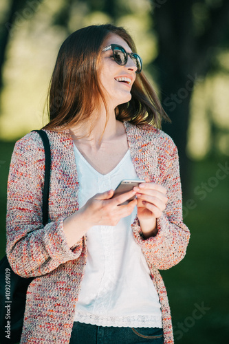 Cute caucasian young woman talking emotional and chat on the phone in the street near green park on spring sunset