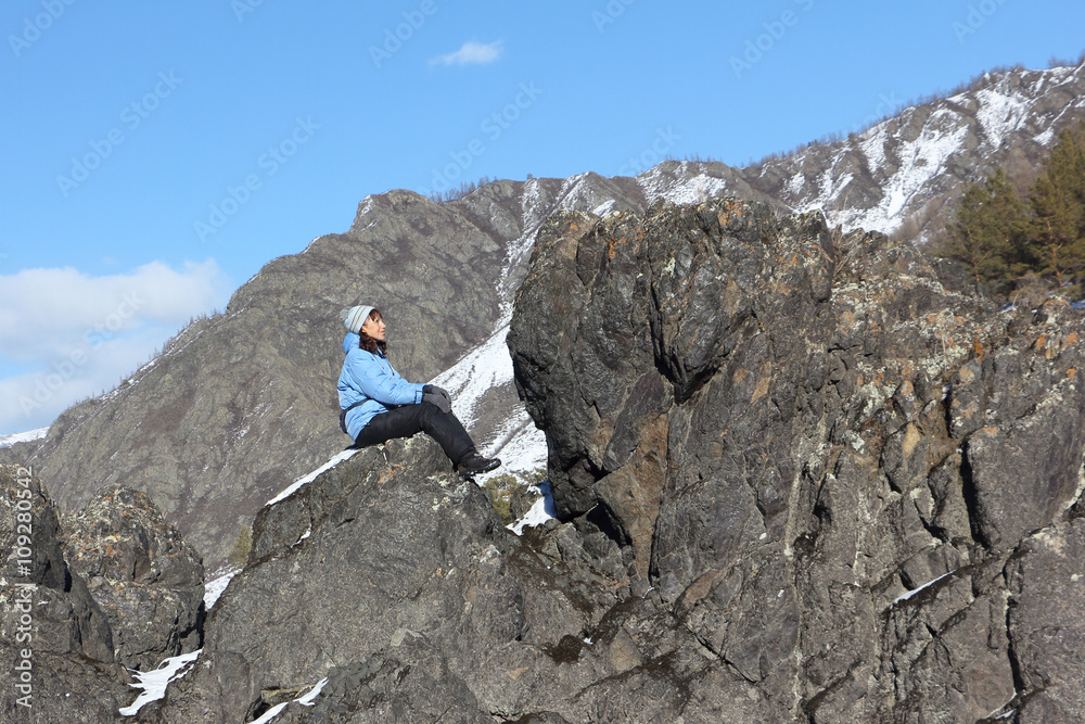 The woman in a blue jacket sitting on the rock