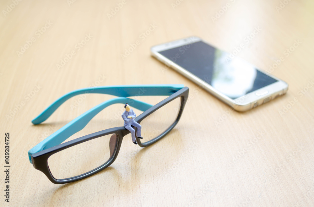 businessman miniature sit on glasses with background of smart ph businessman miniature sit on glasses with background of smart ph