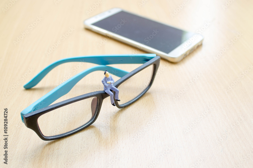 businessman miniature sit on glasses with background of smart ph businessman miniature sit on glasses with background of smart ph