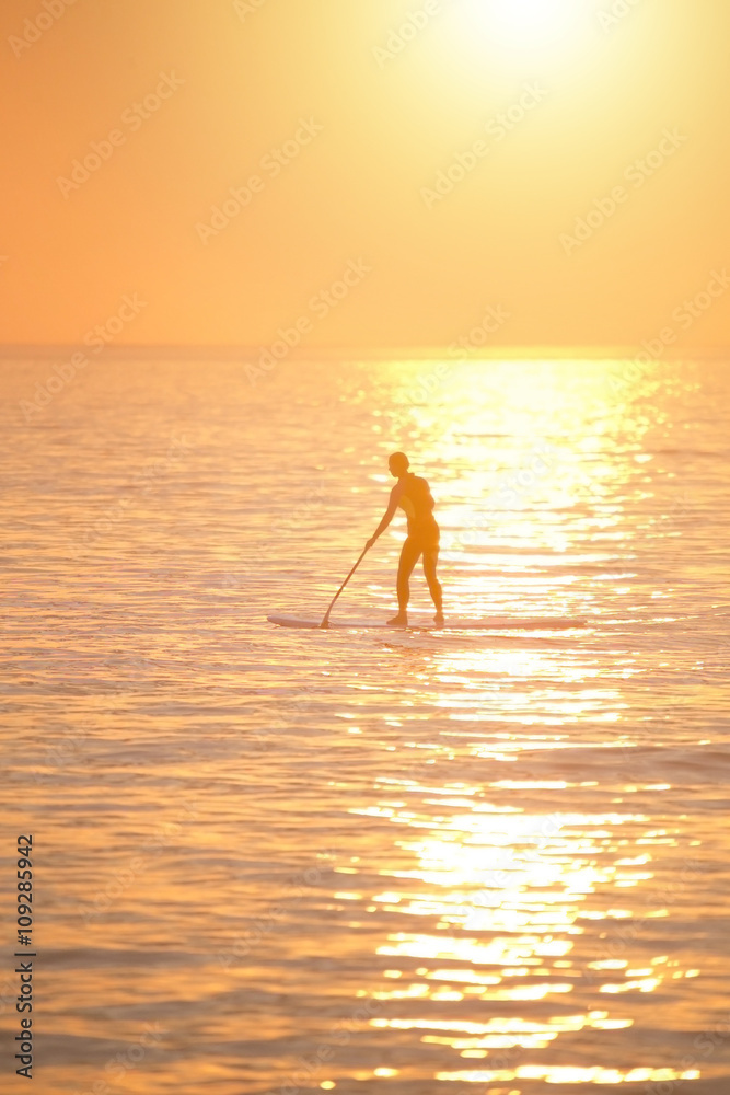 Woman paddle boarding on the sea at stunning orange sunset