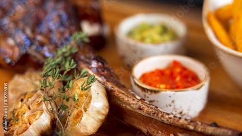 Roasted garlic, guacamole and tomato dip with grilled beef/pork ribs on a wooden table, bbq appetizer