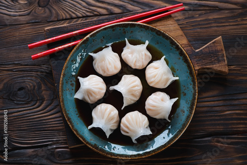 Glass plate with dim-sums in soy sauce, rustic wooden setting