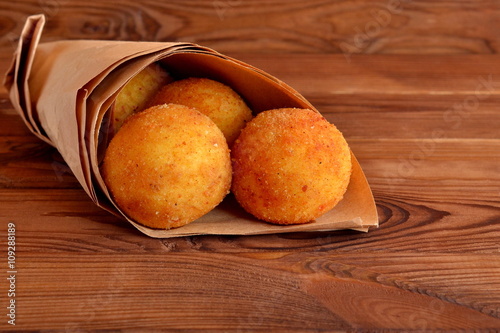 Arancini balls. Fried rice balls in paper on brown wooden background. Snack photo